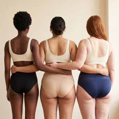 Three women of different sizes seen from the back wearing the shaping briefs in black, beige and navy
