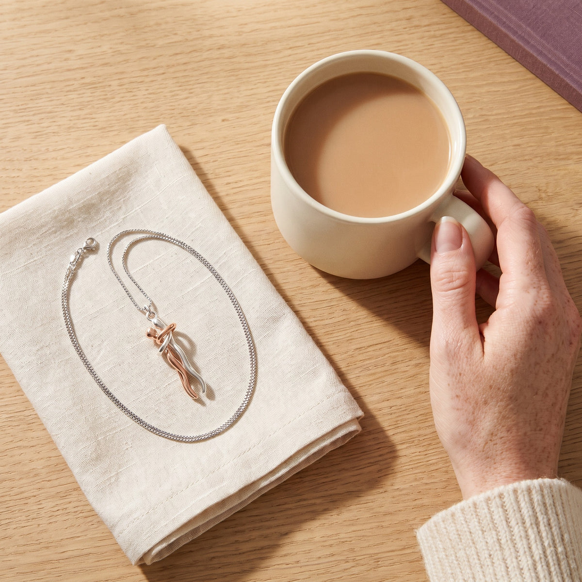 Hug Necklace in rose gold and silver next to a cup of tea