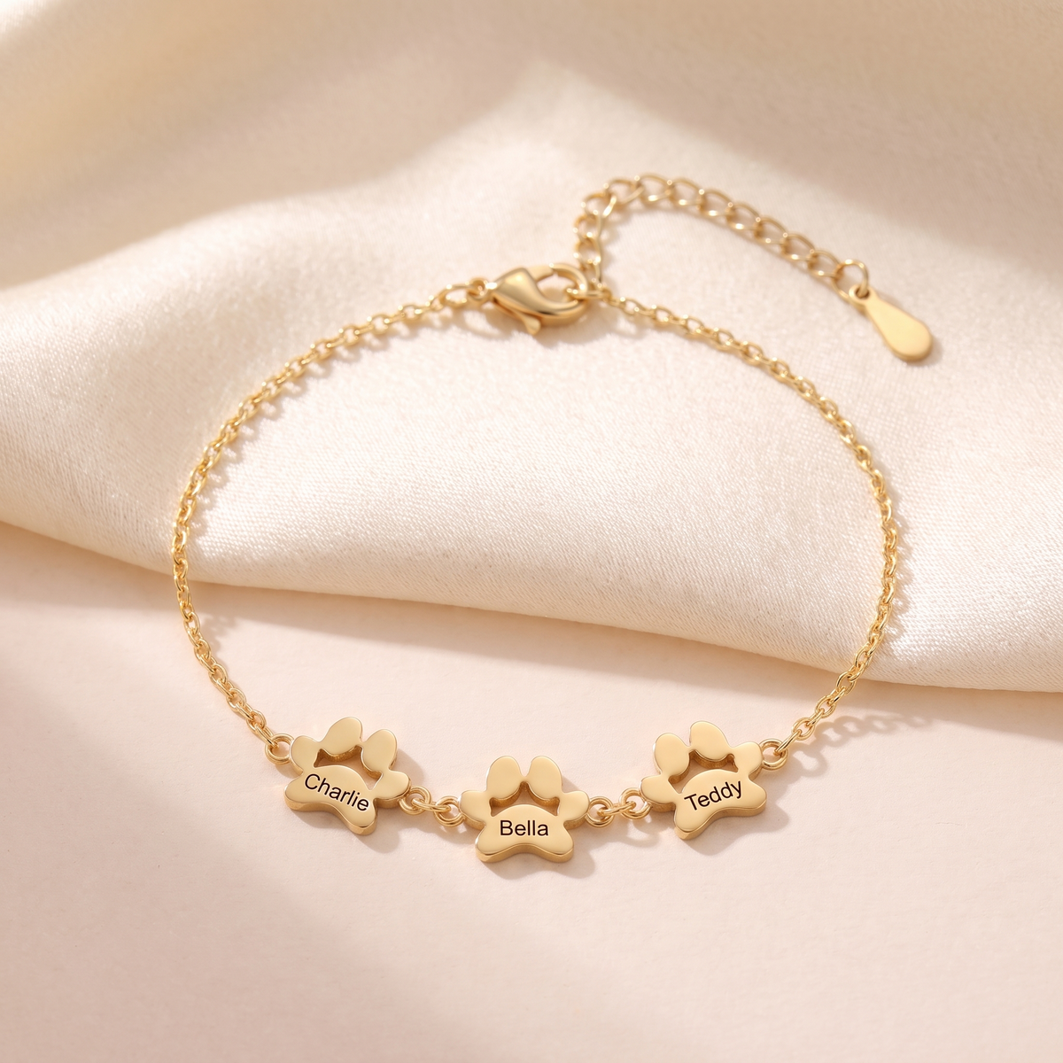 Gold paw print name bracelet engraved Charlie, Bella and Teddy on cream satin