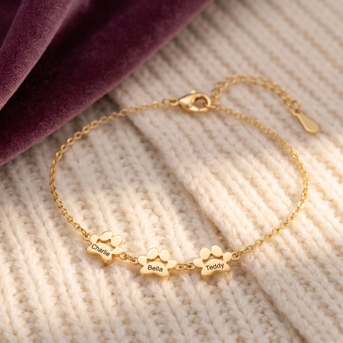 Gold paw print name bracelet engraved Charlie, Bella and Teddy on a cream knit