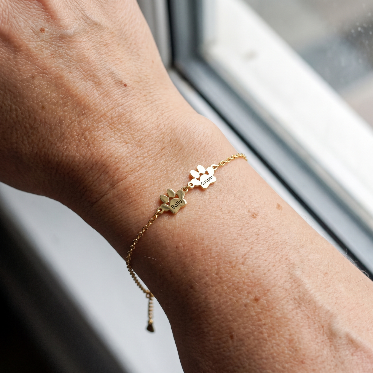 Two small engraved gold paws, Bella and Cooper, on the wrist